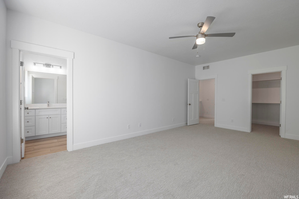 Unfurnished bedroom with a closet, a spacious closet, light colored carpet, ceiling fan, and ensuite bathroom
