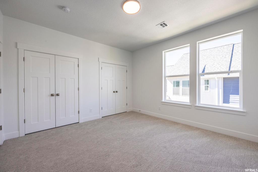 Unfurnished bedroom featuring multiple windows, multiple closets, and light colored carpet