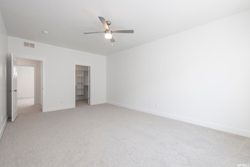 Unfurnished bedroom with ceiling fan, a closet, a spacious closet, and light colored carpet
