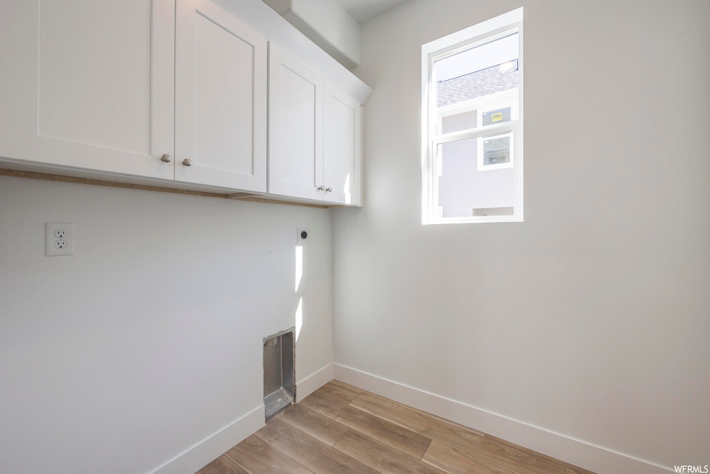 Laundry room featuring light hardwood / wood-style floors, hookup for an electric dryer, and cabinets