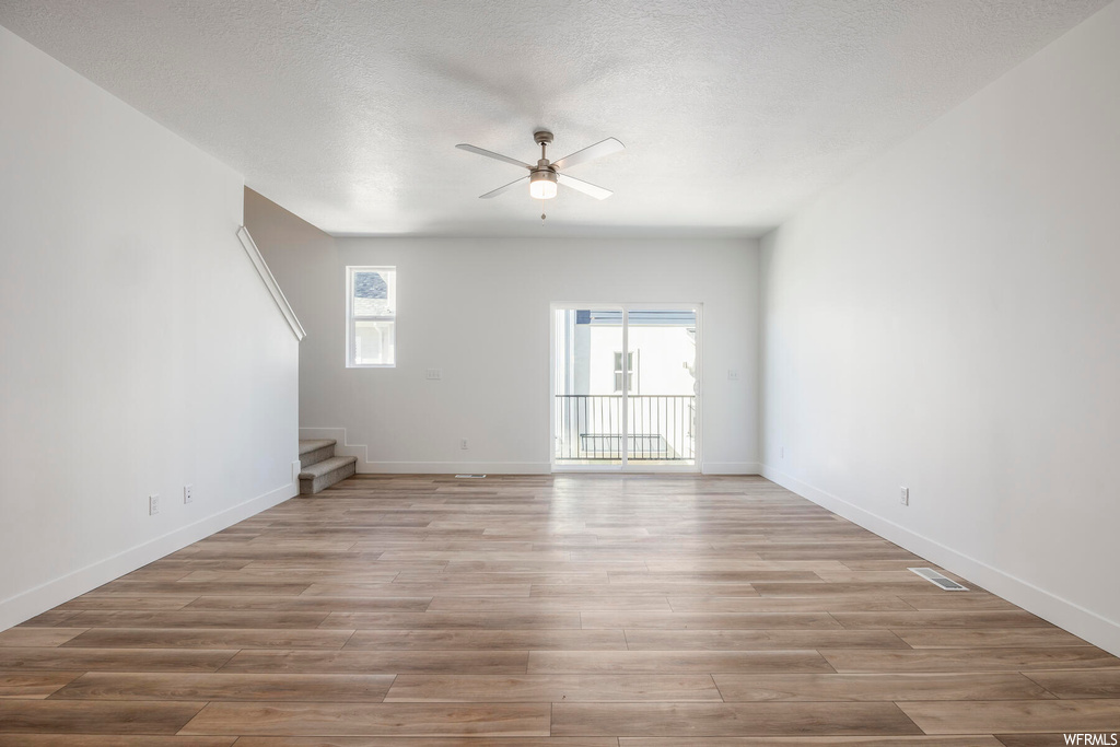 Unfurnished room with light wood-type flooring, ceiling fan, and a textured ceiling