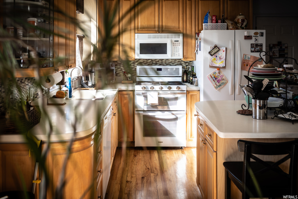 Kitchen featuring white appliances, hardwood / wood-style floors, tasteful backsplash, and sink