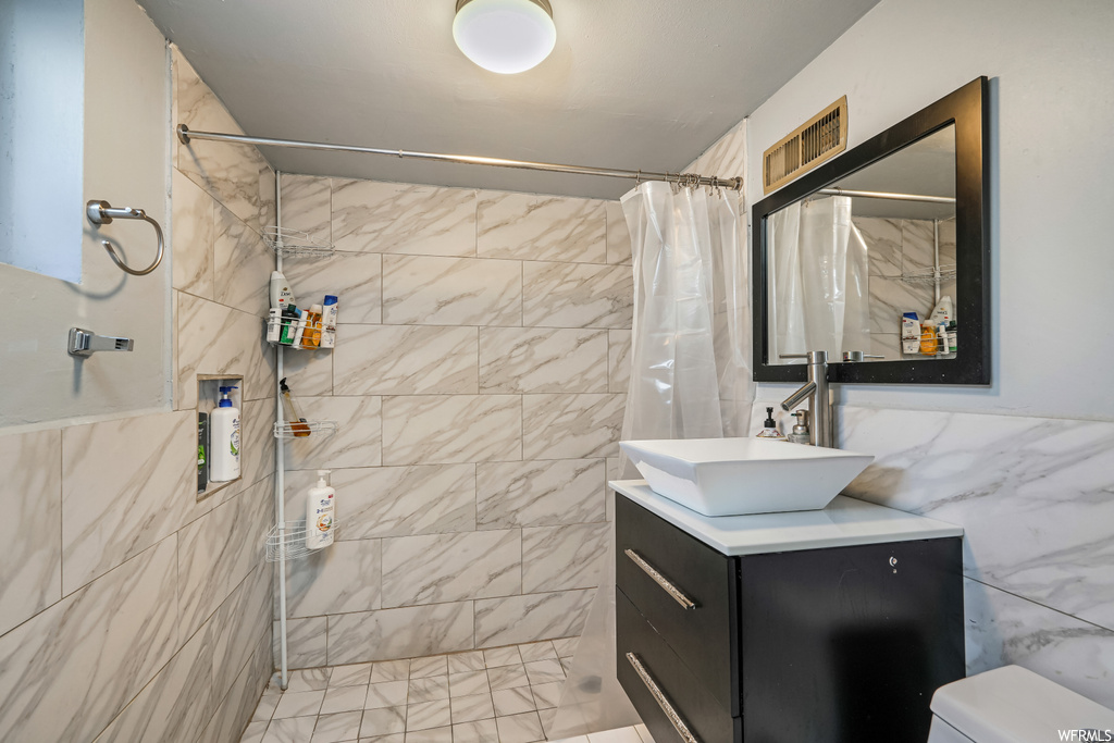 Bathroom featuring tile walls, oversized vanity, toilet, and walk in shower