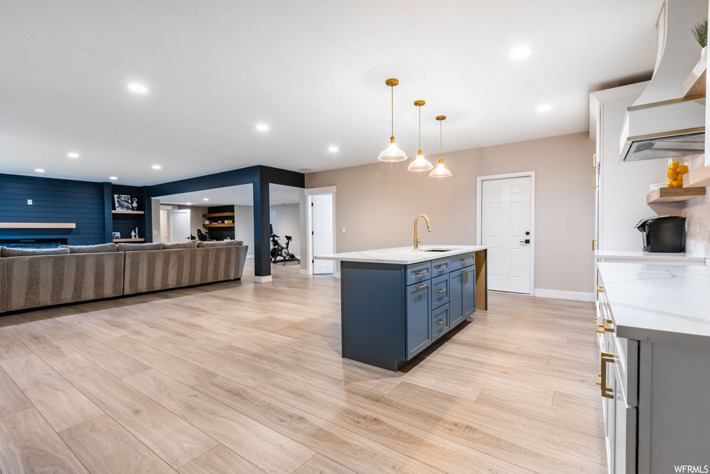 Kitchen featuring a center island with sink, sink, light hardwood / wood-style flooring, pendant lighting, and custom range hood