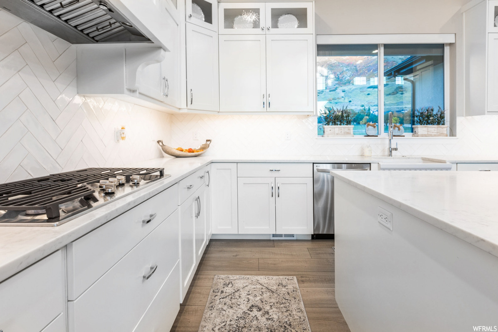 Kitchen featuring appliances with stainless steel finishes, custom range hood, white cabinetry, and tasteful backsplash