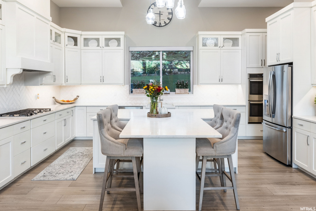 Kitchen featuring a center island, light hardwood / wood-style floors, tasteful backsplash, white cabinets, and premium range hood