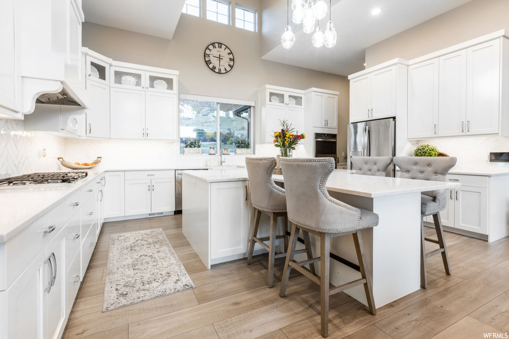 Kitchen with a center island, backsplash, stainless steel appliances, white cabinets, and pendant lighting