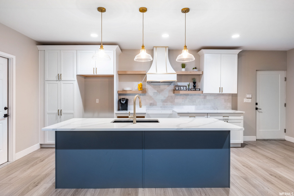 Kitchen with white cabinetry, tasteful backsplash, a kitchen island with sink, and custom range hood