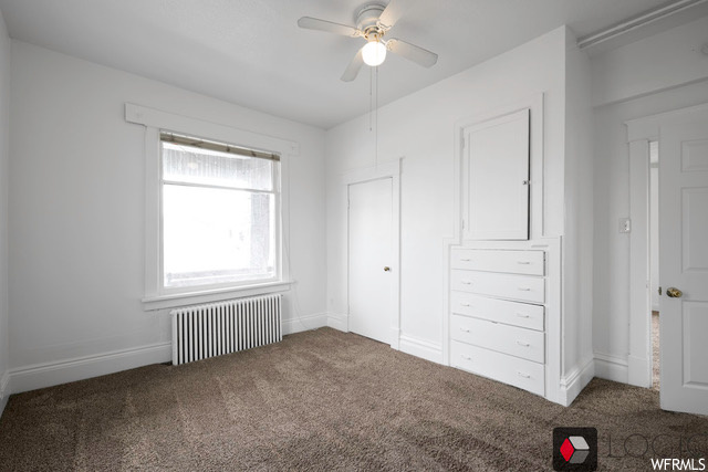 Unfurnished bedroom featuring radiator heating unit, dark carpet, and ceiling fan