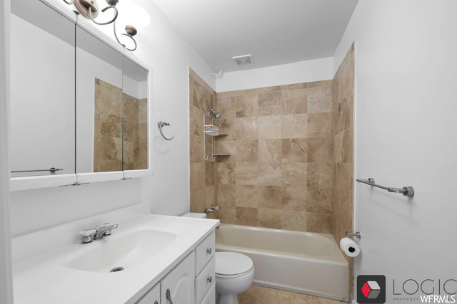 Full bathroom with toilet, vanity, tiled shower / bath combo, and tile flooring