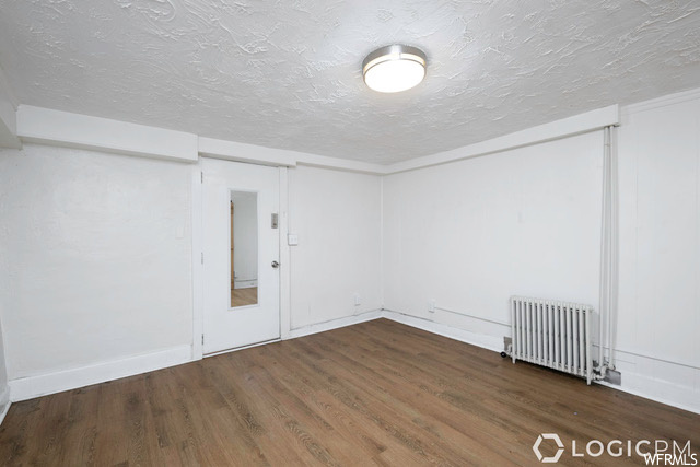 Empty room featuring a textured ceiling, dark hardwood flooring, and radiator