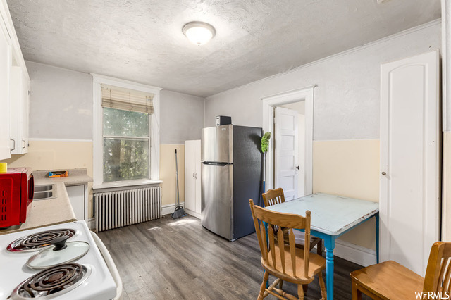 Kitchen with range, radiator, stainless steel refrigerator, dark hardwood floors, and white cabinetry