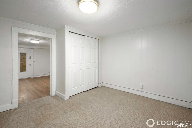 Unfurnished bedroom with a baseboard radiator, light carpet, crown molding, and a closet