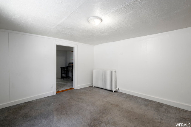 Spare room featuring a textured ceiling, radiator heating unit, and carpet floors