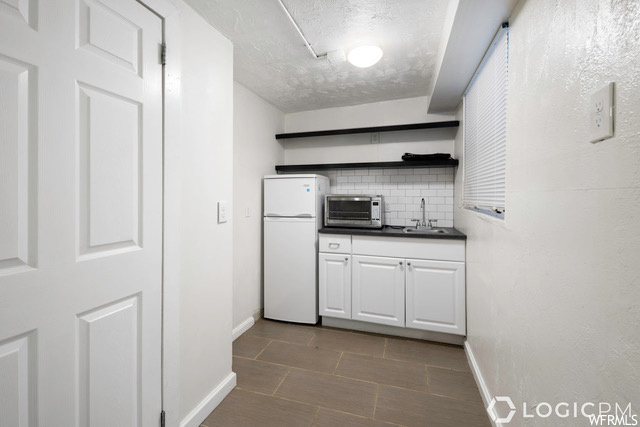 Kitchen with sink, white cabinets, backsplash, white fridge, and dark tile floors