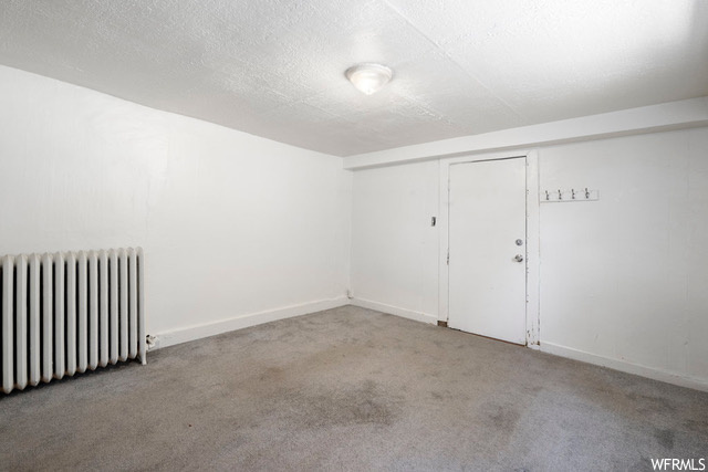 Unfurnished room with light carpet, a textured ceiling, and radiator heating unit