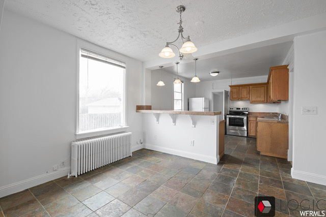 Kitchen with white fridge, radiator heating unit, stove, dark tile flooring, and an inviting chandelier