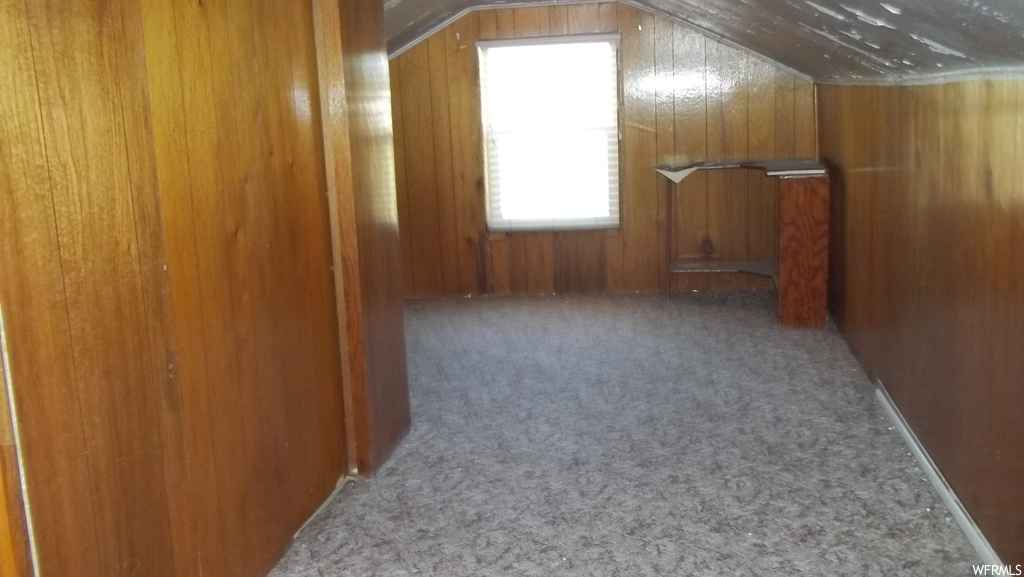 Additional living space with vaulted ceiling, wood walls, and carpet