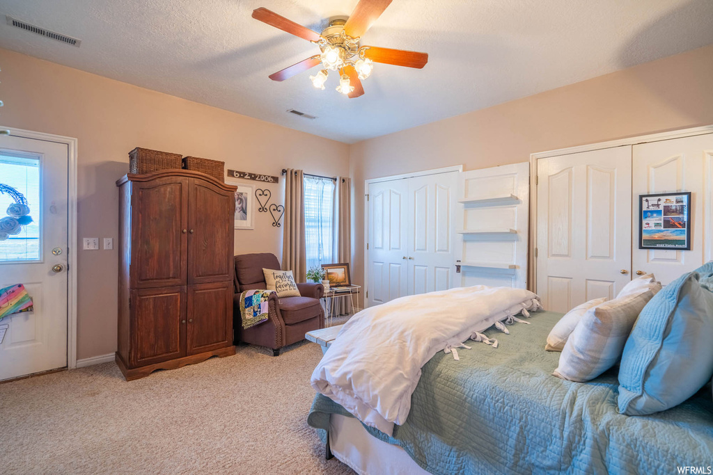 Bedroom featuring multiple closets, light carpet, multiple windows, and ceiling fan