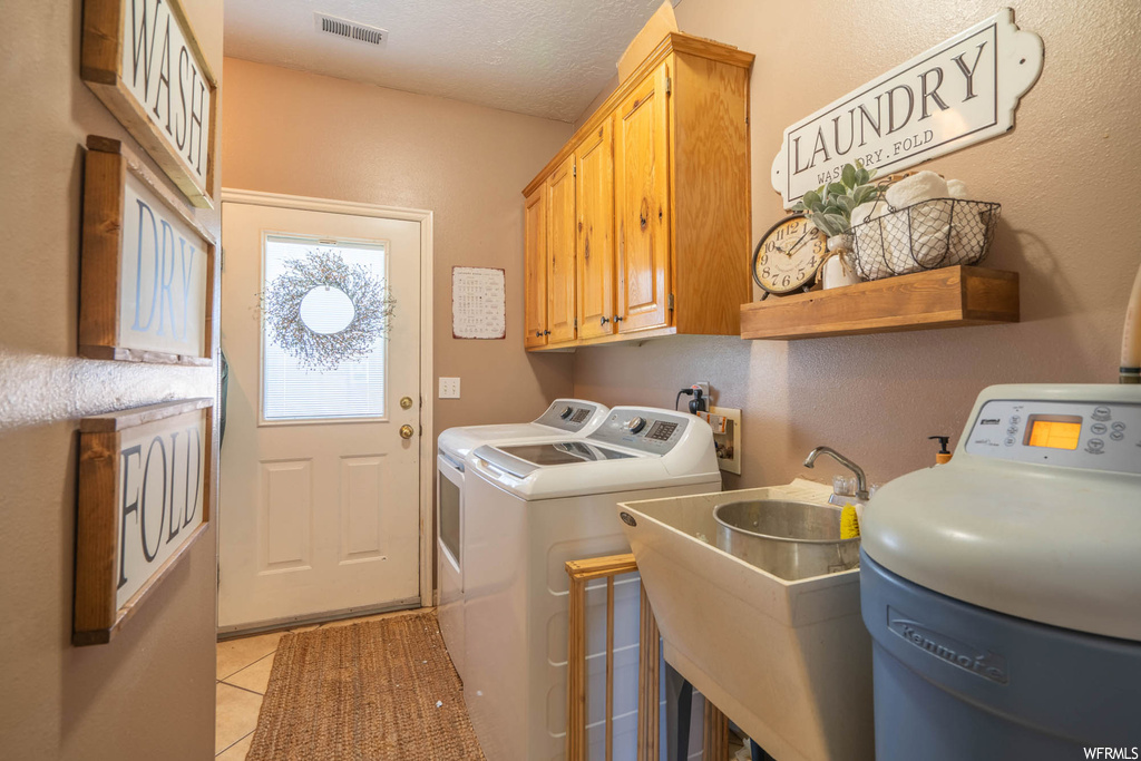 Washroom featuring sink, a textured ceiling, cabinets, light tile flooring, and separate washer and dryer