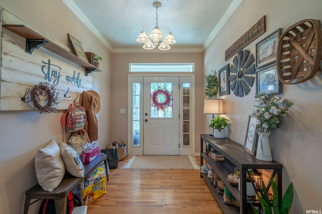 Entryway with a textured ceiling, crown molding, a notable chandelier, and light hardwood / wood-style flooring