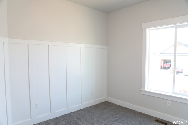 Unfurnished room featuring a wealth of natural light and dark carpet