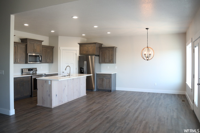 Kitchen featuring decorative light fixtures, dark hardwood / wood-style floors, an island with sink, stainless steel appliances, and an inviting chandelier
