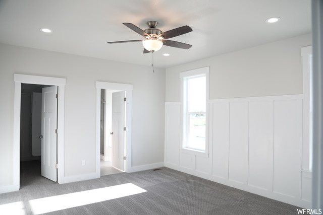 Unfurnished bedroom with connected bathroom, ceiling fan, a spacious closet, and light colored carpet