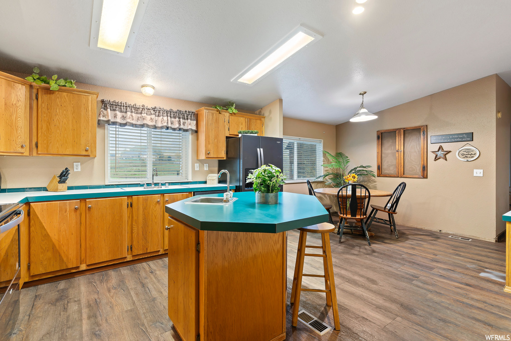 Kitchen featuring dark hardwood flooring, hanging light fixtures, stainless steel refrigerator with ice dispenser, and a kitchen island with sink