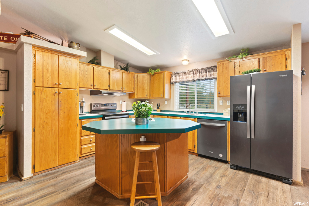 Kitchen with a breakfast bar, vaulted ceiling, light hardwood floors, a center island, and stainless steel appliances