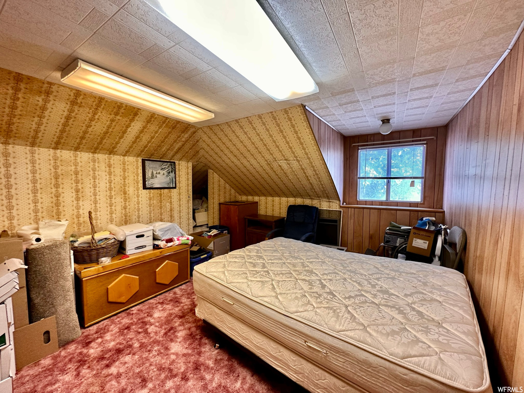 Carpeted bedroom featuring wood walls and lofted ceiling