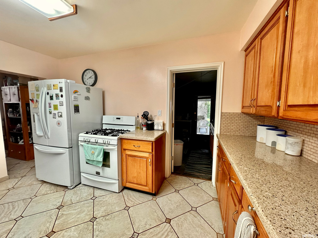 Kitchen featuring white appliances, backsplash, light tile floors, and light stone counters