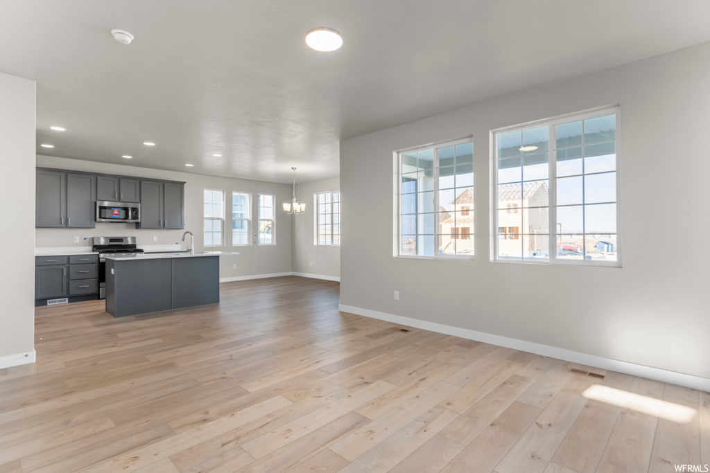 Kitchen featuring a wealth of natural light, appliances with stainless steel finishes, an island with sink, and light hardwood / wood-style flooring