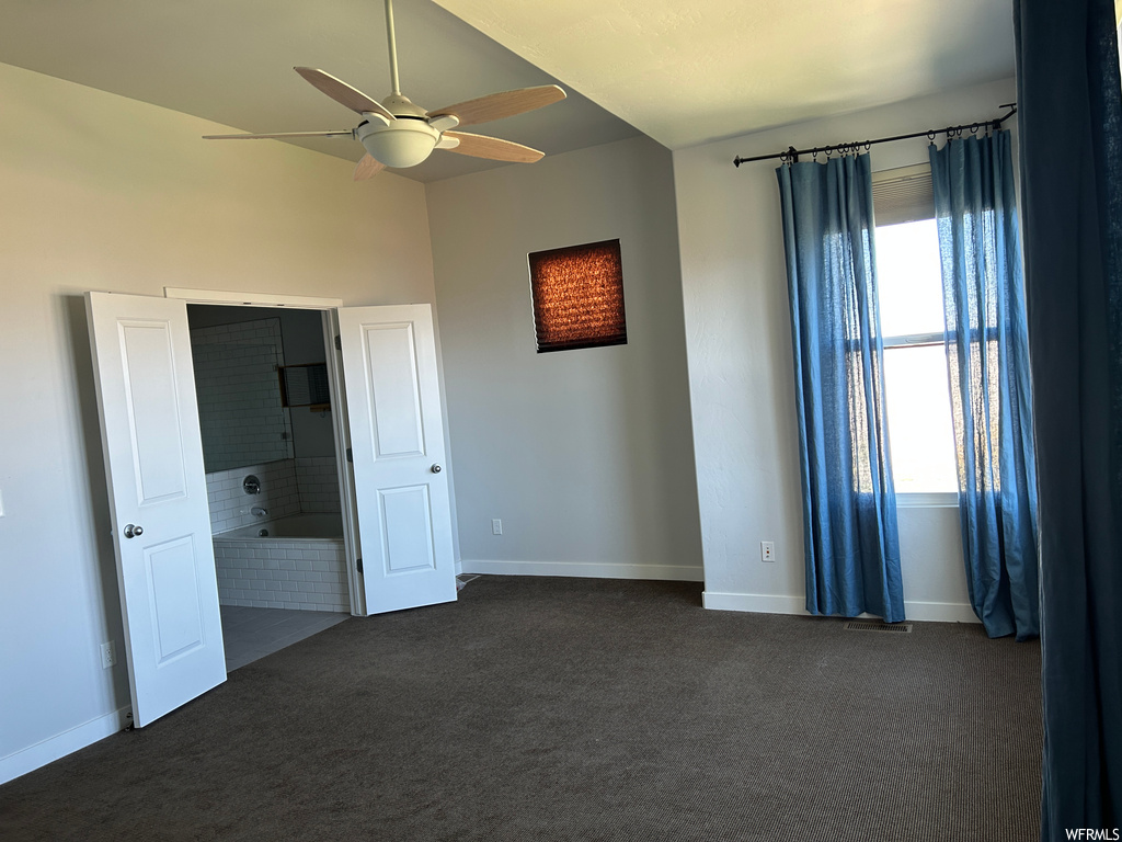 Spare room featuring ceiling fan, a wealth of natural light, and dark colored carpet