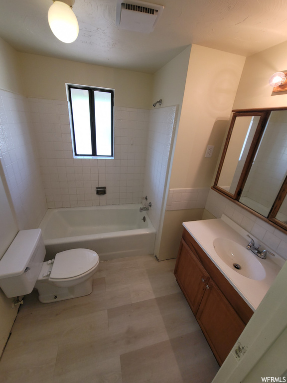 Full bathroom with toilet, tile floors, large vanity, backsplash, and tiled shower / bath