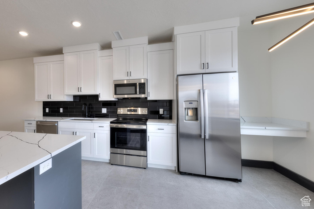 Kitchen featuring stainless steel appliances, light stone counters, white cabinetry, sink, and light tile floors
