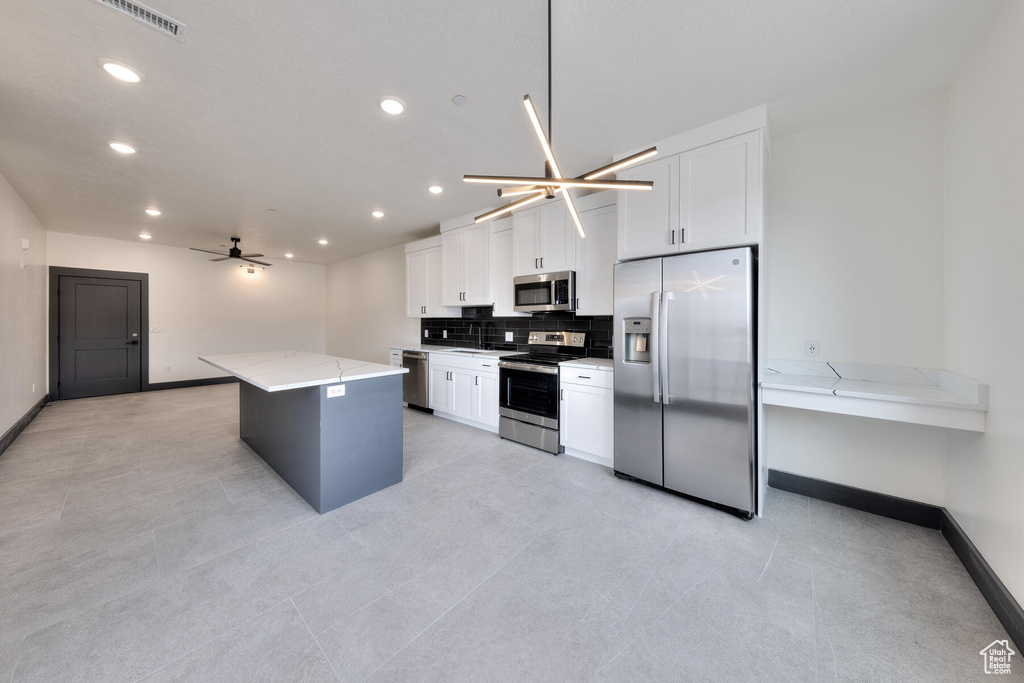 Kitchen featuring white cabinets, a center island, light stone countertops, and stainless steel appliances