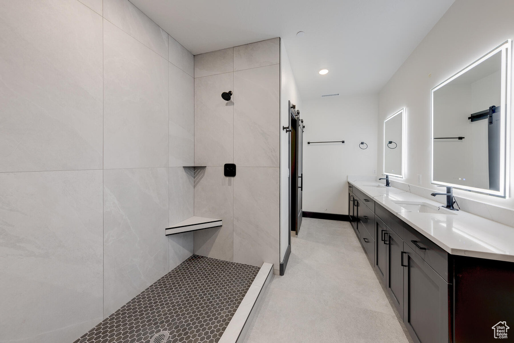 Bathroom with double sink, tile flooring, a tile shower, and vanity with extensive cabinet space