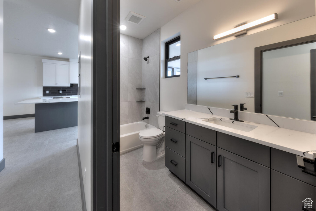 Full bathroom with tiled shower / bath, vanity, backsplash, toilet, and tile floors