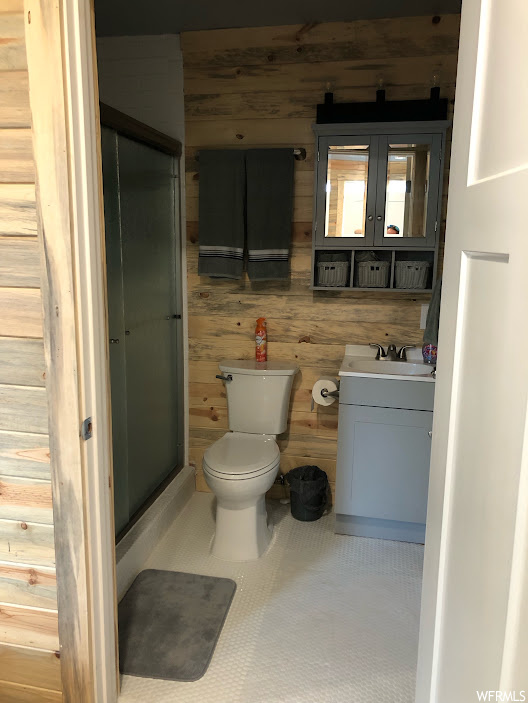 Bathroom featuring an enclosed shower, toilet, vanity, and wood walls