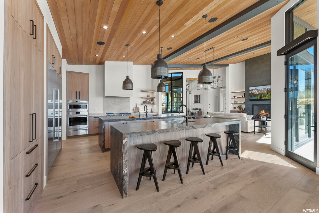 Kitchen with decorative light fixtures, light hardwood / wood-style flooring, a kitchen bar, and wood ceiling