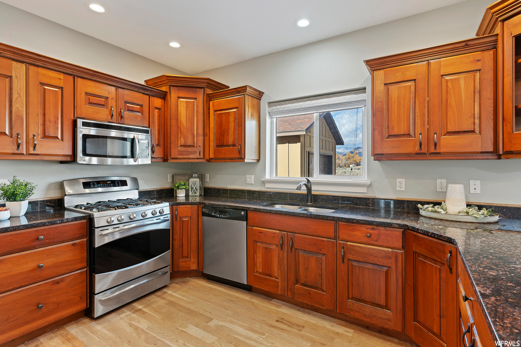 Kitchen featuring stainless steel appliances, light wood-type flooring, dark stone countertops, and sink