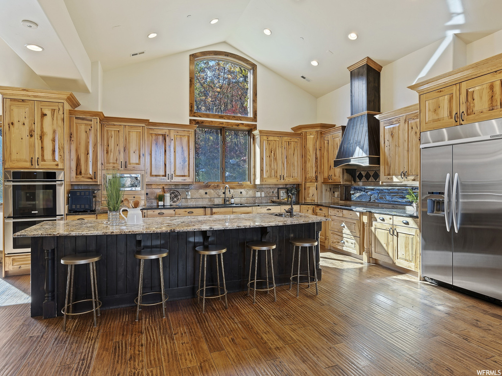 Kitchen with a large island with sink, light stone countertops, dark hardwood / wood-style floors, high vaulted ceiling, and custom range hood