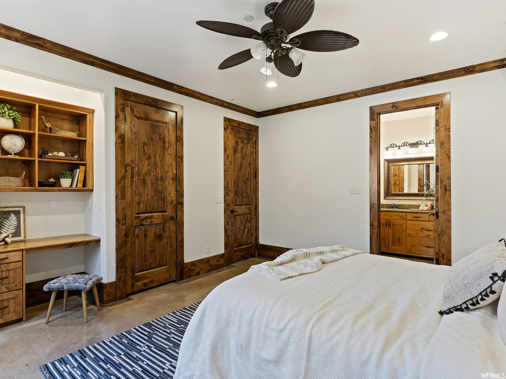 Carpeted bedroom featuring ceiling fan, ornamental molding, ensuite bathroom, and built in desk