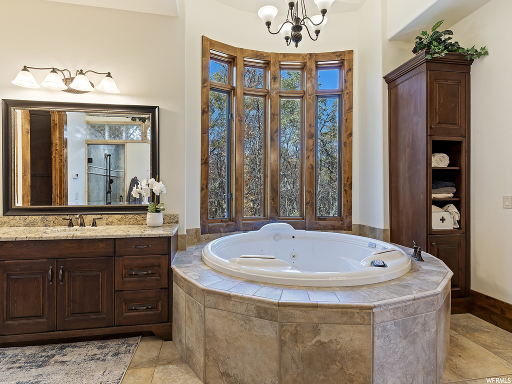 Bathroom with a relaxing tiled bath, an inviting chandelier, large vanity, and tile flooring
