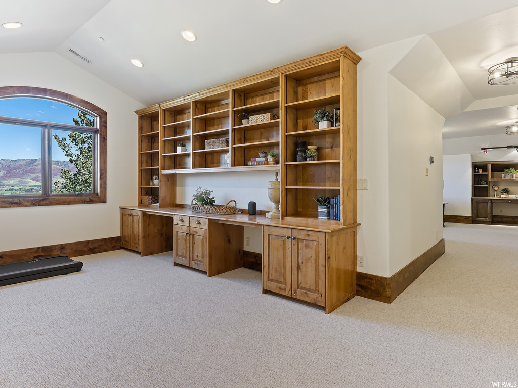 Carpeted home office featuring built in desk and vaulted ceiling