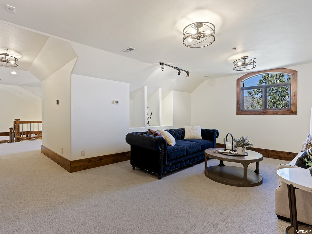 Carpeted living room with lofted ceiling, track lighting, and a notable chandelier