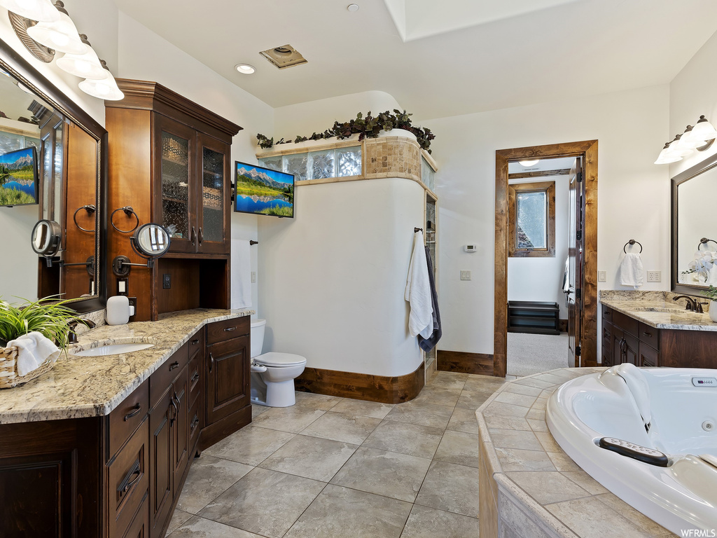 Bathroom featuring dual vanity, tiled tub, toilet, and tile floors