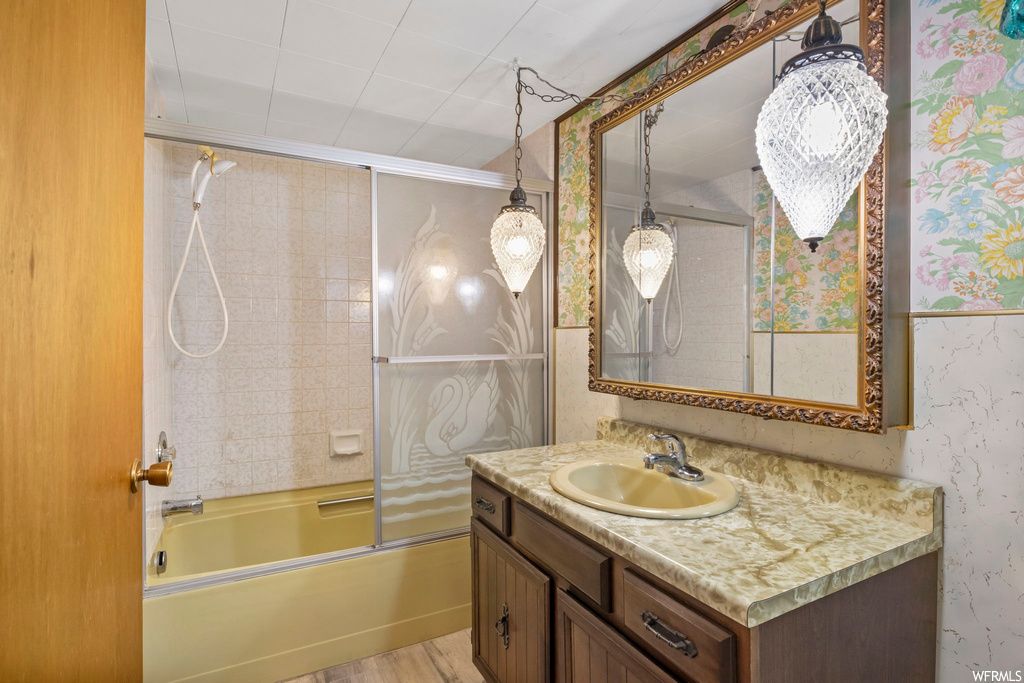 Bathroom with combined bath / shower with glass door, hardwood / wood-style floors, and vanity