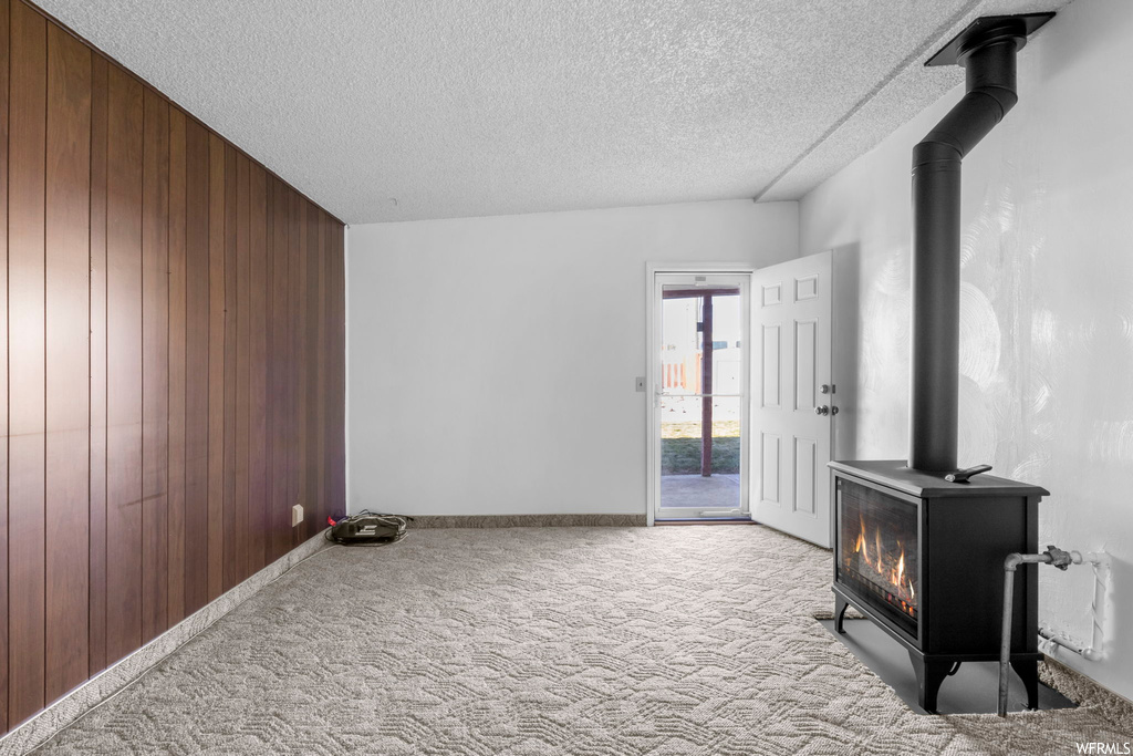 Carpeted empty room featuring a wood stove, wooden walls, and a textured ceiling
